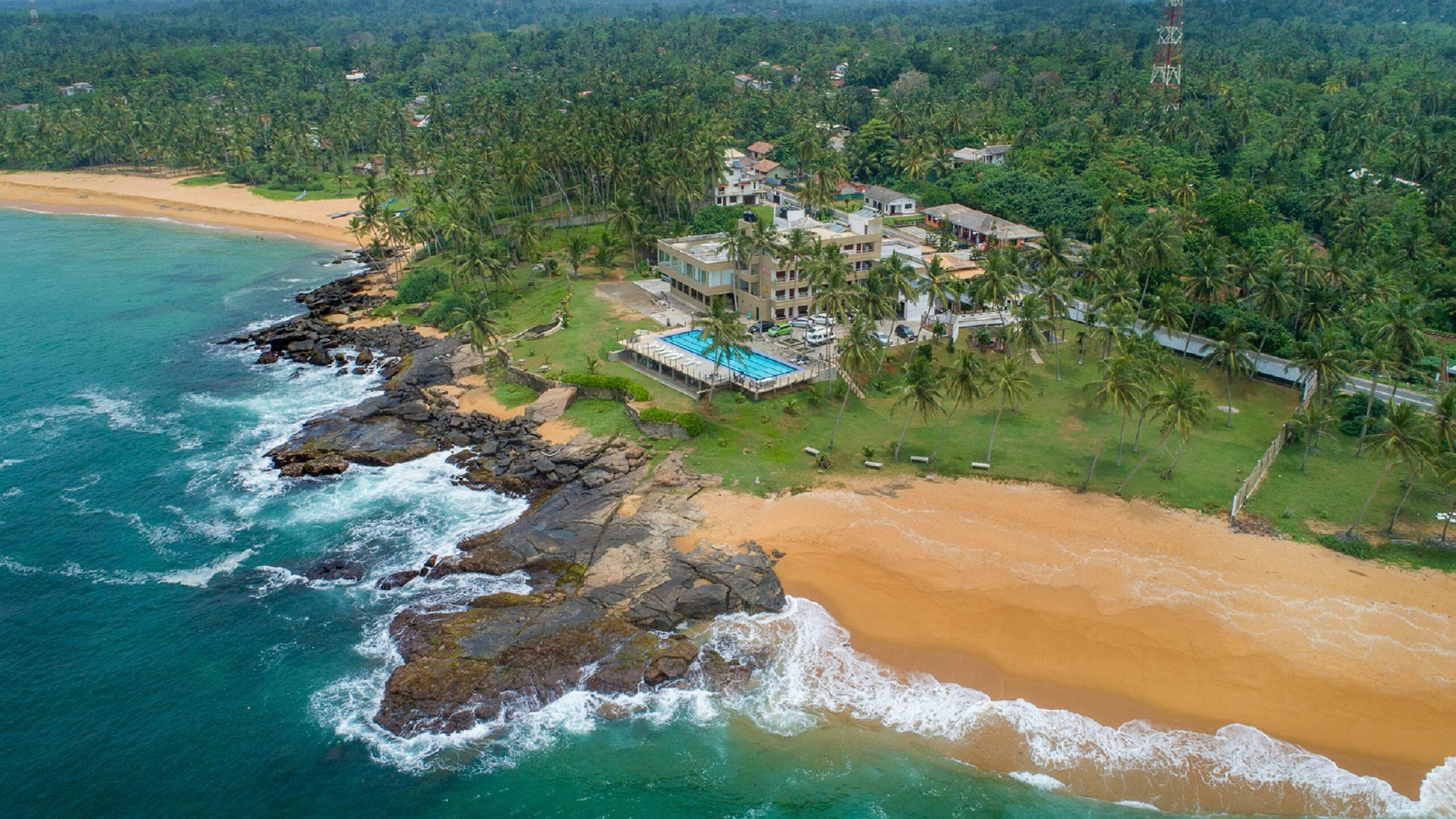 An aerial view of Hikkaduwa Beach in Sri Lanka, which is a great place for a family holiday to Sri Lanka and features golden sand beaches, verdant coconut trees, and blue ocean waves.