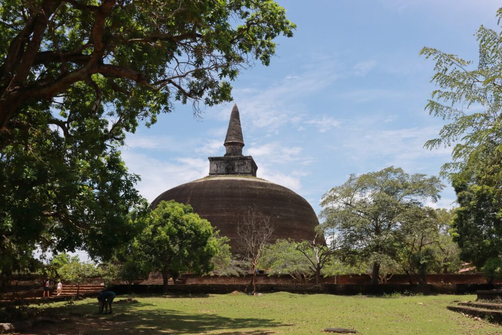 This stupa is Rankoth Vihara in Polonnaruwa, Sri Lanka. The stupa has a dome-shaped structure with a pointed apex and is likely located in a temple complex.