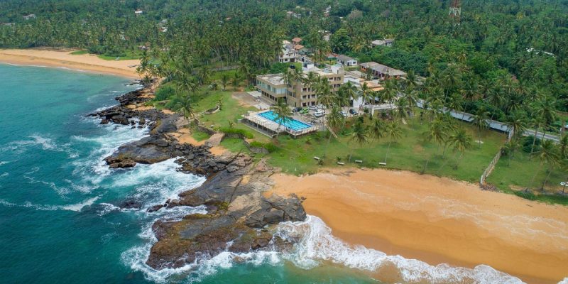 An aerial view of Hikkaduwa Beach in Sri Lanka, which is a great place for a family holiday to Sri Lanka and features golden sand beaches, verdant coconut trees, and blue ocean waves.